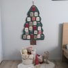 Grand calendrier de l'Avent mural en tissu vert foncé en forme de sapin avec poches numérotées aux motifs de Noël. Ambiance de chambre d'enfant avec corbeille de peluches, gnome rouge et renne en bois.