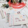 Ensemble de pochettes en tissu pour la Lettre au Père Noël fabriquées à la main par Coudcoeurcie, ornées de timbres illustrés et de finitions en tissu vichy et fleuri sur fond blanc étoilé.