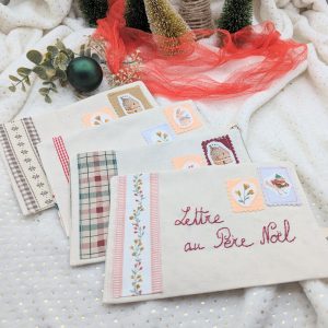 Ensemble de pochettes en tissu pour la Lettre au Père Noël fabriquées à la main par Coudcoeurcie, ornées de timbres illustrés et de finitions en tissu vichy et fleuri sur fond blanc étoilé.